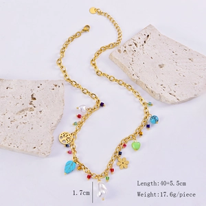 Detail view of gold titanium necklace with tree of life, flower, and pearl charms on white stones