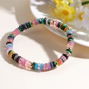 Colorful semi-precious stone bead bracelet with gold accents on a white floral background