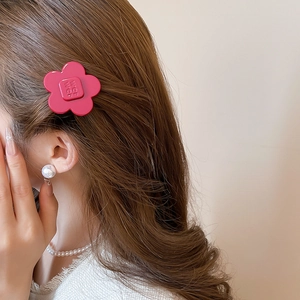 Close-up of red resin flower hair clip with W.P letter detail on model side profile
