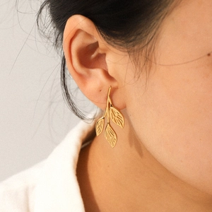 18K gold-plated stainless steel leaf branch earrings with textured vein detailing on model