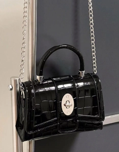 Detail view of glossy crocodile pattern handbag with silver twist lock and chain strap