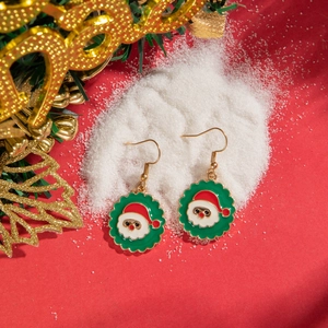 Close-up of green Santa Claus earrings on artificial snow with festive red background
