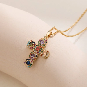 Vue macro d'un collier croix doré avec zircons multicolores sertis sur un support blanc