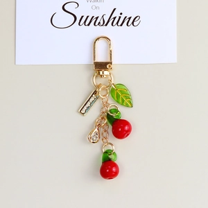 Close-up of a cherry keychain with red beads, green leaf, and gold D-ring clasp