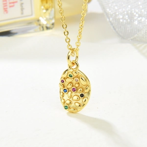 Gold oval pendant necklace with colorful zircons and hammered texture on white background