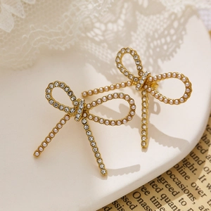 Macro detail of gold bow earrings featuring pavé rhinestones and a white faux pearl