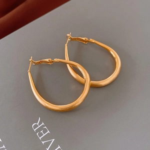 Macro shot of gold-plated oval hoop earrings with a brushed matte metallic finish