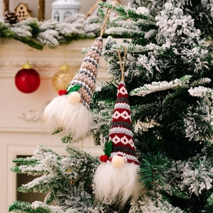 Detail of knitted Christmas gnome ornaments with led lights hanging on a snowy tree