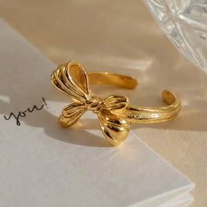 18k gold plated stainless steel bow ring with textured weave design on beige background