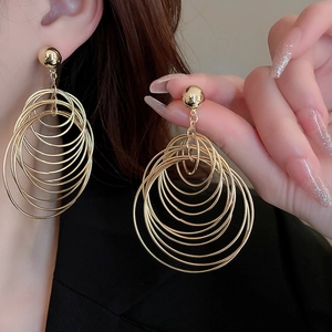 Detailed close-up of layered golden hoop earrings being held to show the scale and texture
