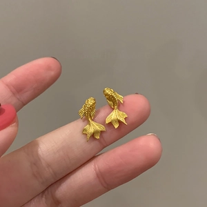Gros plan de boucles d'oreilles carpe koi dorées 18 carats avec texture mate et détails