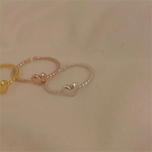 Close-up of heart charm rings with twisted and beaded texture in gold, rose gold and silver