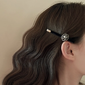 Detailed view of a velvet camellia hair clip with pearl and gold accents in wavy brown hair