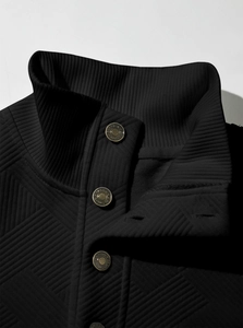 Detail of black diamond-pattern quilted fabric with branded metal snap buttons and ribbed collar