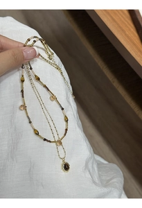 Detail of layered gold-plated necklace featuring brown tiger eye stone pendant