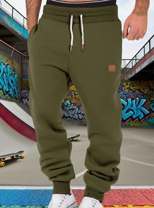 Detail of olive green joggers featuring a drawstring elastic waist and leather patch logo