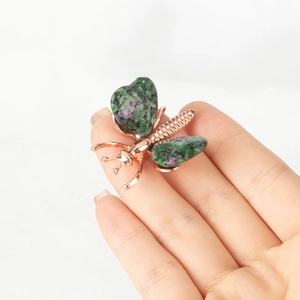 Detailed macro view of a rose gold butterfly brooch with natural green and pink stone wings