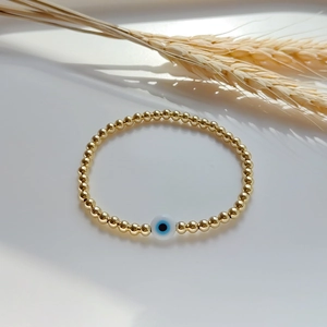 Detail of gold beaded bracelet with a blue evil eye charm against white background