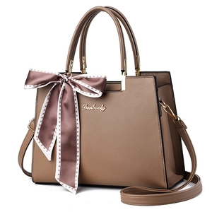 Sac à main en cuir marron texturé avec accents dorés et ruban décoratif sur fond blanc