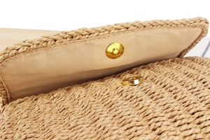 Detail view of the golden magnetic closure and textured straw weaving of the crossbody bag