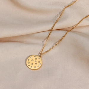 Detailed view of a gold round pendant necklace with sparkling crystals on beige satin fabric