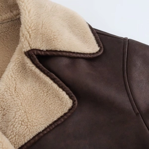 Detail of a brown leather jacket featuring a thick beige shearling collar and stitching