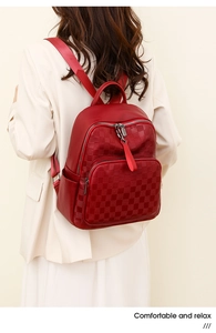 Red leather backpack with embossed checkerboard texture shown on model in ivory suit