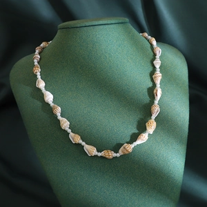 Detail of handmade seashell necklace with white beads on dark green velvet display