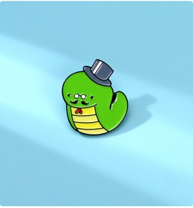 Detail of green cartoon snake enamel pin with top hat, mustache and red bow tie