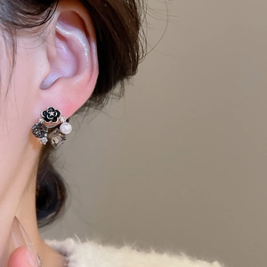 Dettaglio di orecchini a fiore con perle, smalto nero e cristalli grigi indossati