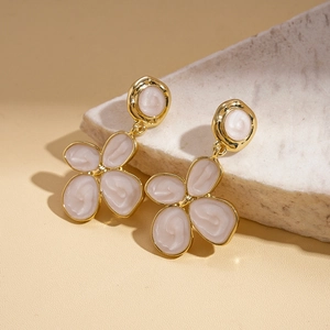 Detail of elegant gold flower earrings with white enamel petals on a stone surface