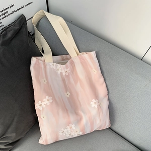 Détail du sac cabas en toile dégradé rose avec broderie florale sur un canapé gris