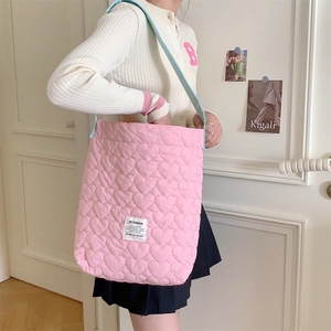 Close-up of pink heart-quilted shoulder bag with blue contrast strap and brand tag