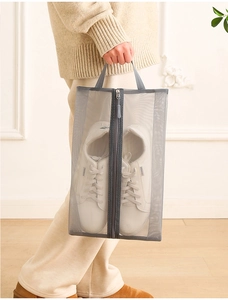 Handheld view of a grey mesh travel shoe bag with a middle zipper and portable handle