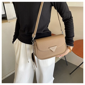 Détail d'un sac carré en cuir marron avec motif litchi, rabat triangle et bandoulière réglable