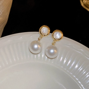 Detail of gold-plated pearl drop earrings with round shell inlay on a white ceramic plate