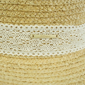 Detailed macro view of woven straw sun hat with elegant lace ribbon and gold nameplate