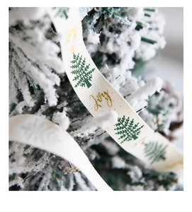 Macro detail of Christmas ribbon with green trees and golden Joy print on snowy tree