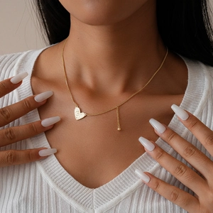 Detail of a gold textured heart pendant necklace worn on a white ribbed sweater