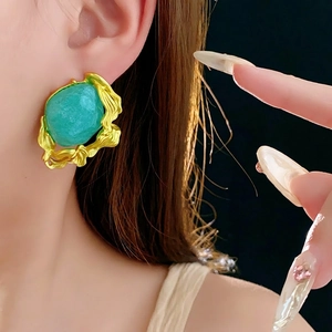 Vintage emerald-style turquoise studs with irregular gold-tone trim worn by a model