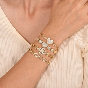 Detail view of four-piece gold bracelet set with white zircon hearts and clovers worn on wrist