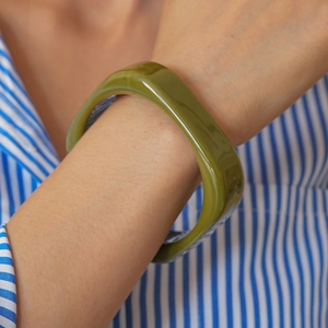 Close-up of a wide green resin square bangle on a model wearing a striped shirt