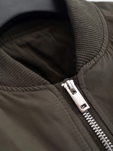 Detailed close-up of army green bomber jacket neckline with ribbing and silver metal zipper