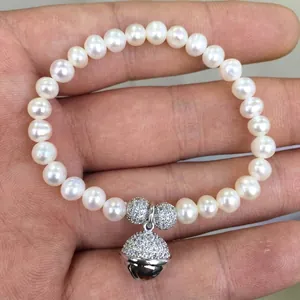 Close-up of white freshwater pearl bracelet with micro-pave bell pendant and diamond beads