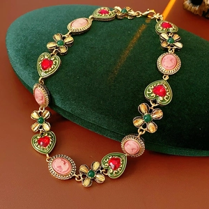 Détail macro d'un collier vintage doré avec cœurs en émail et incrustations florales