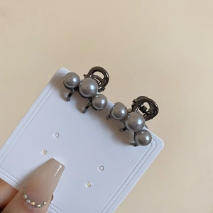 Detailed view of two mini dark grey pearl hair claws on a card held by hand