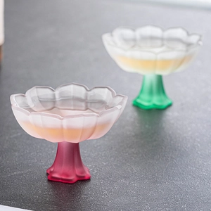 Elegant lotus-shaped frosted glass tea cups in pink and green on a dark textured surface