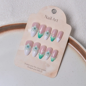 Detail of almond nails with 3D floral patterns and French tips on a cream display card