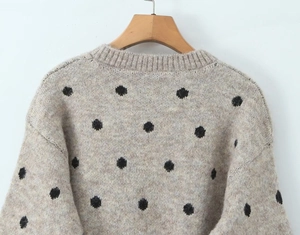 Dettaglio di un maglione in maglia beige a pois neri con scollo rotondo a coste