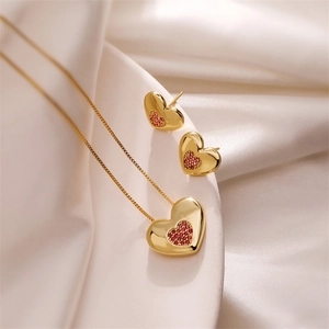 Close-up of gold heart pendant necklace and earrings set with red zircon inlay